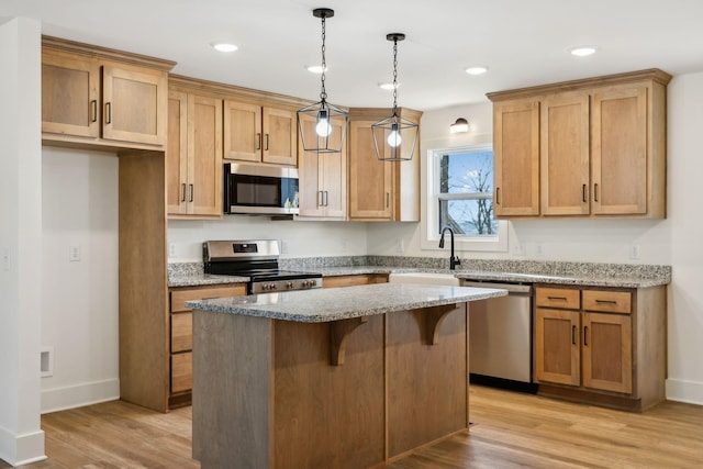 kitchen featuring sink, appliances with stainless steel finishes, decorative light fixtures, a kitchen island, and light stone counters