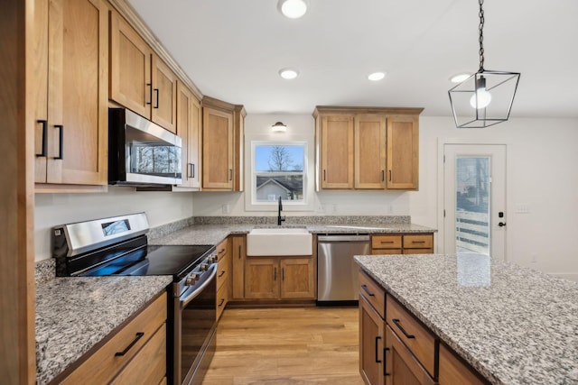 kitchen featuring light stone countertops, light wood-type flooring, stainless steel appliances, sink, and hanging light fixtures