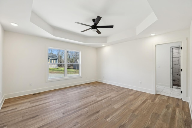 unfurnished room featuring a tray ceiling, ceiling fan, and light hardwood / wood-style floors