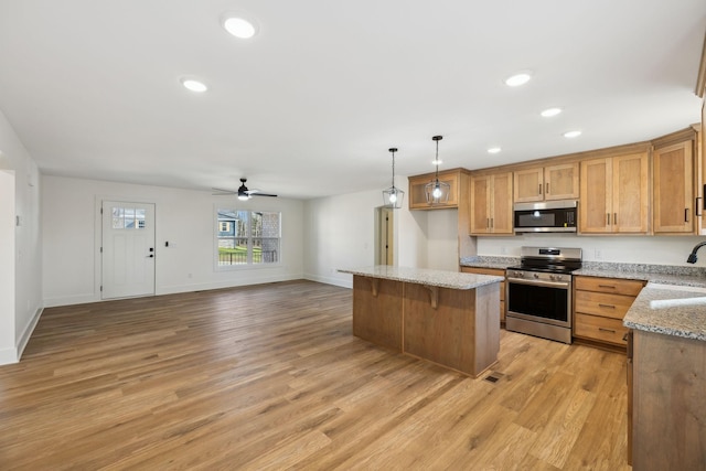 kitchen featuring light wood-type flooring, stainless steel appliances, ceiling fan, sink, and hanging light fixtures