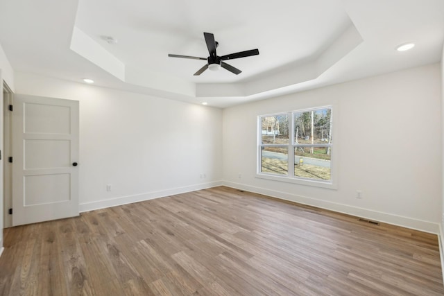 spare room with ceiling fan, light hardwood / wood-style flooring, and a tray ceiling