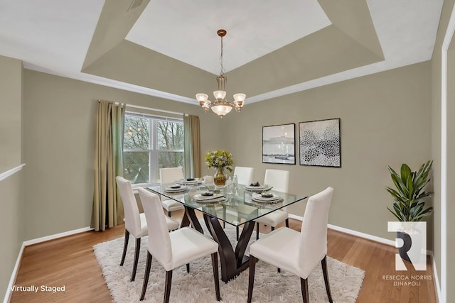 dining space featuring a raised ceiling, light hardwood / wood-style flooring, and a notable chandelier