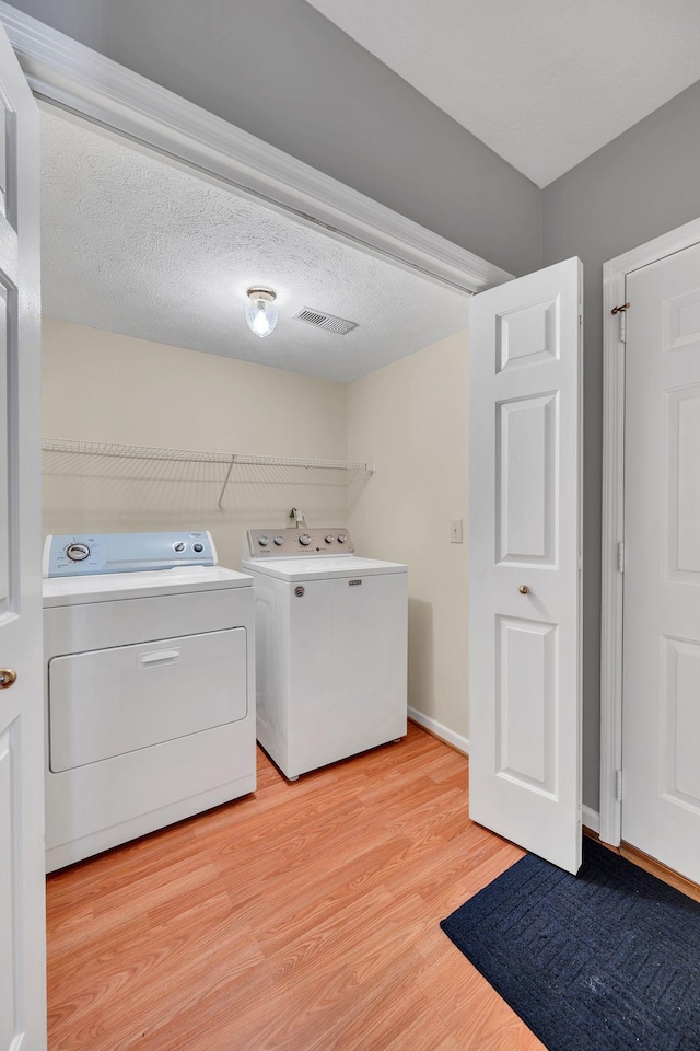 laundry room featuring washer and dryer, a textured ceiling, and light wood-type flooring