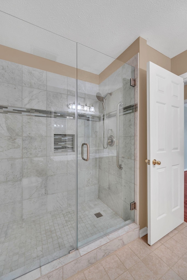 bathroom with tile patterned floors, a shower with door, and a textured ceiling