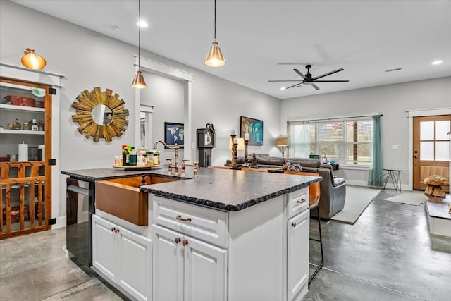 kitchen with a kitchen island with sink, sink, concrete flooring, decorative light fixtures, and white cabinetry