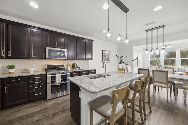 kitchen featuring sink, a kitchen breakfast bar, hanging light fixtures, stainless steel appliances, and a center island with sink