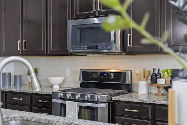 kitchen with dark brown cabinetry, appliances with stainless steel finishes, light stone countertops, and decorative backsplash