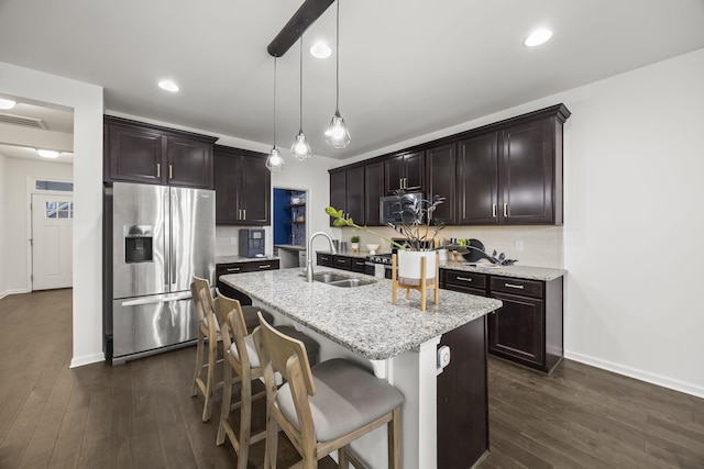 kitchen with sink, decorative light fixtures, an island with sink, stainless steel appliances, and light stone countertops