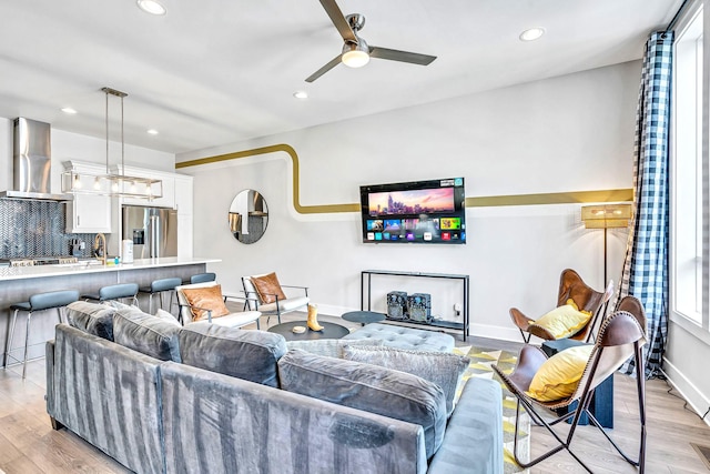 living room with light wood-type flooring, ceiling fan, and sink