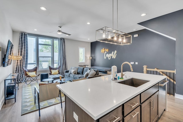 kitchen with a center island with sink, ceiling fan, sink, and light hardwood / wood-style flooring