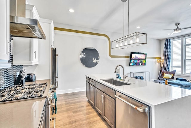 kitchen featuring sink, hanging light fixtures, stainless steel appliances, wall chimney range hood, and a center island with sink