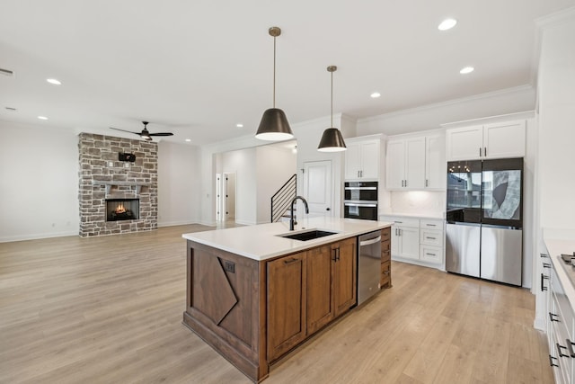 kitchen featuring white cabinets, sink, a fireplace, an island with sink, and decorative light fixtures