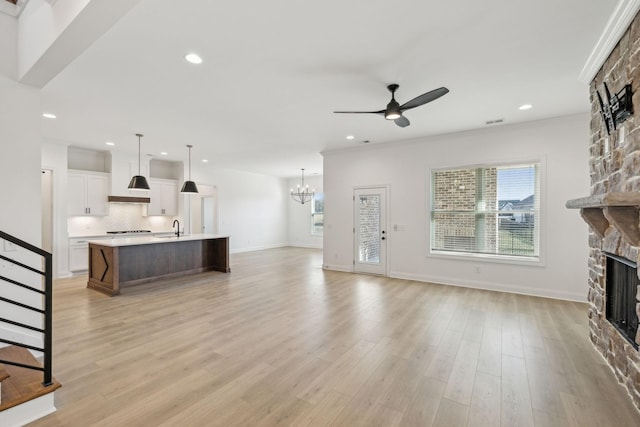 living room featuring ornamental molding, ceiling fan with notable chandelier, sink, a fireplace, and light hardwood / wood-style floors