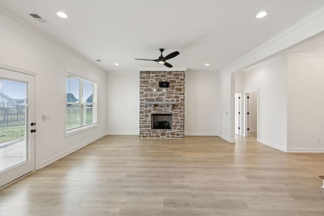 unfurnished living room with light wood-type flooring, a stone fireplace, ceiling fan, and crown molding