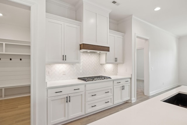 kitchen featuring stainless steel gas stovetop, white cabinets, crown molding, light hardwood / wood-style flooring, and decorative backsplash