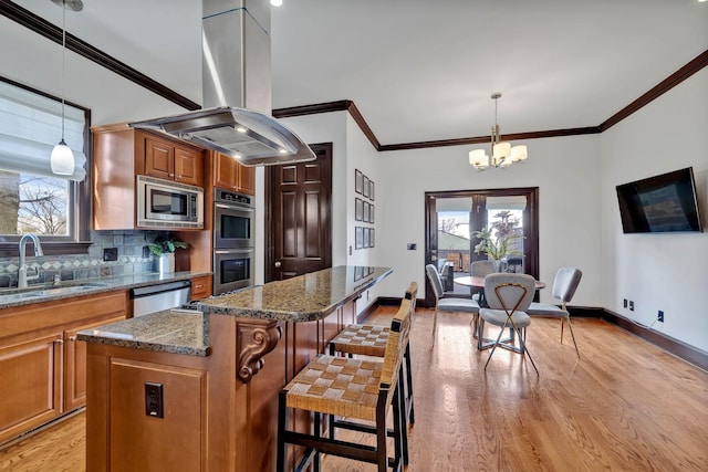 kitchen with appliances with stainless steel finishes, island range hood, sink, decorative light fixtures, and a kitchen island