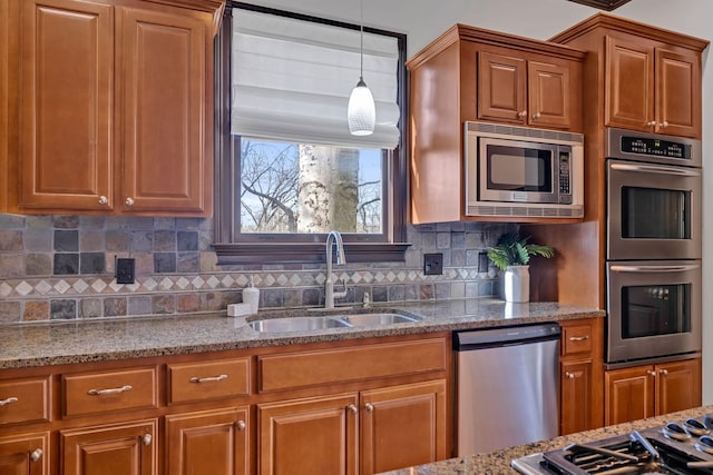 kitchen featuring light stone countertops, appliances with stainless steel finishes, tasteful backsplash, sink, and decorative light fixtures