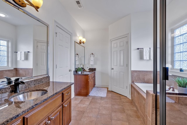 bathroom with tile patterned floors, tiled tub, and vanity