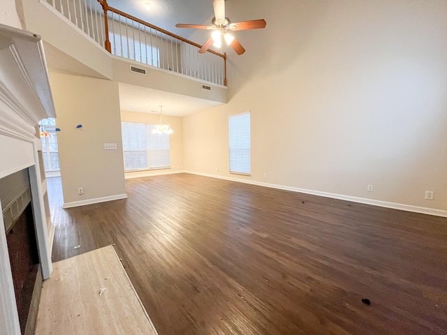 unfurnished living room featuring ceiling fan with notable chandelier, dark hardwood / wood-style floors, and a high ceiling