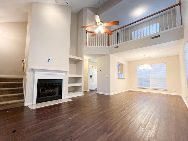 unfurnished living room featuring ceiling fan with notable chandelier, built in shelves, a towering ceiling, and dark wood-type flooring