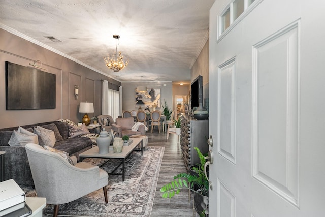 living room with a notable chandelier, hardwood / wood-style floors, ornamental molding, and a textured ceiling