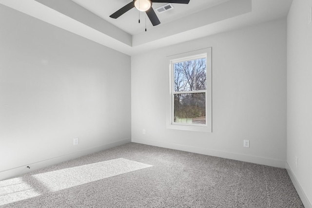 empty room featuring a tray ceiling, ceiling fan, and carpet floors