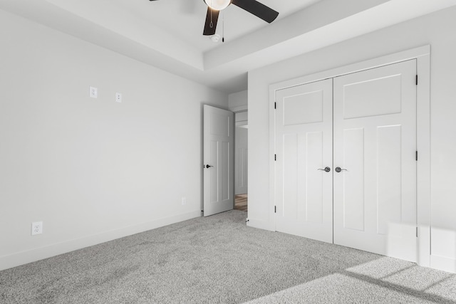 unfurnished bedroom featuring a tray ceiling, ceiling fan, a closet, and carpet