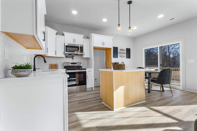 kitchen with appliances with stainless steel finishes, sink, a center island, white cabinetry, and hanging light fixtures