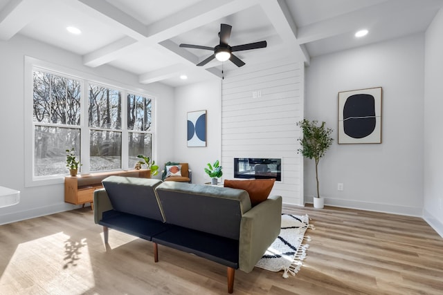 living room featuring coffered ceiling, light hardwood / wood-style flooring, ceiling fan, a fireplace, and beamed ceiling