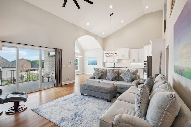 living room with a wealth of natural light, light hardwood / wood-style flooring, high vaulted ceiling, and ceiling fan with notable chandelier