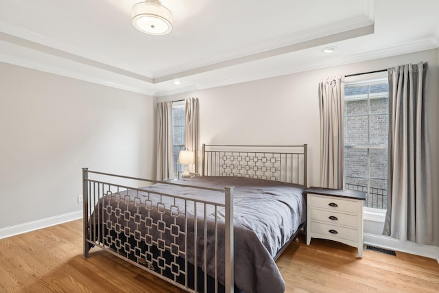 bedroom featuring a tray ceiling, light hardwood / wood-style floors, and ornamental molding