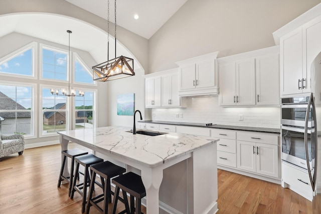 kitchen featuring sink, hanging light fixtures, dark stone countertops, an island with sink, and white cabinets