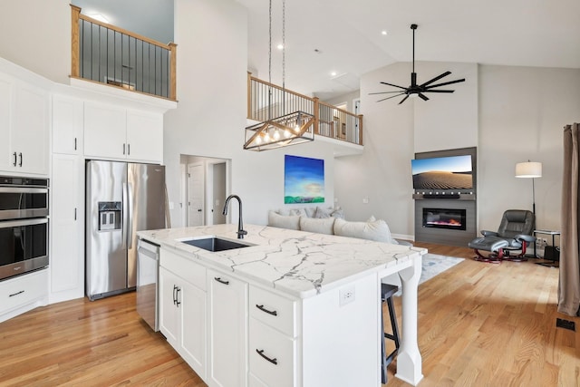 kitchen with a kitchen island with sink, white cabinets, sink, ceiling fan, and appliances with stainless steel finishes