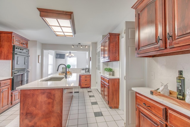 kitchen with sink, black double oven, a chandelier, a center island with sink, and light tile patterned flooring