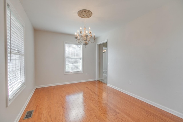 empty room with hardwood / wood-style floors and a notable chandelier