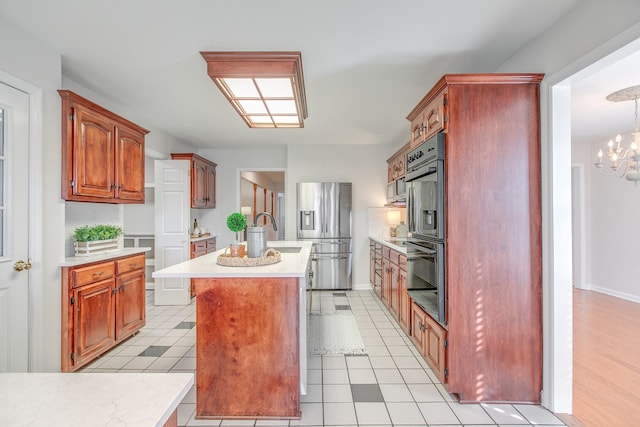 kitchen featuring stainless steel refrigerator with ice dispenser, black double oven, light tile patterned floors, a notable chandelier, and an island with sink