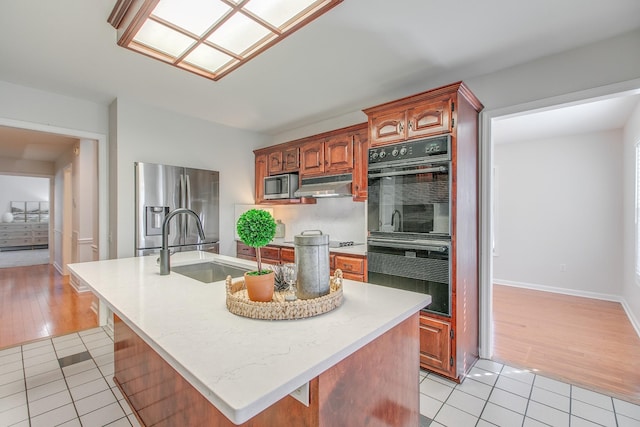 kitchen with light tile patterned flooring, appliances with stainless steel finishes, sink, and an island with sink