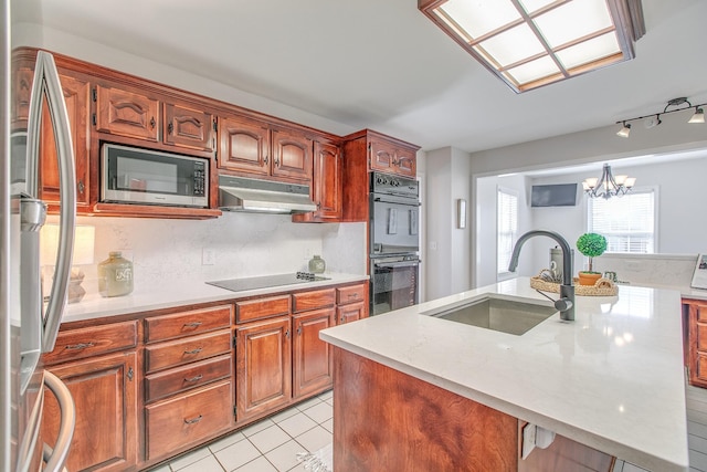 kitchen featuring a kitchen island with sink, black appliances, sink, a notable chandelier, and light tile patterned flooring