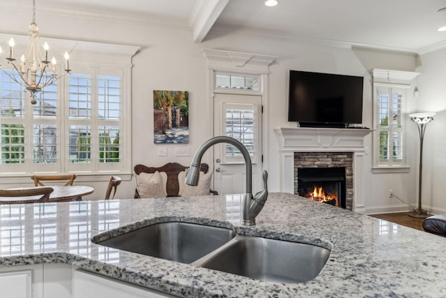 kitchen featuring sink, hanging light fixtures, a fireplace, white cabinets, and ornamental molding