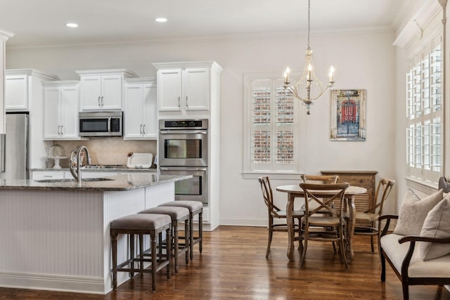 kitchen with white cabinets, sink, dark stone countertops, ornamental molding, and stainless steel appliances