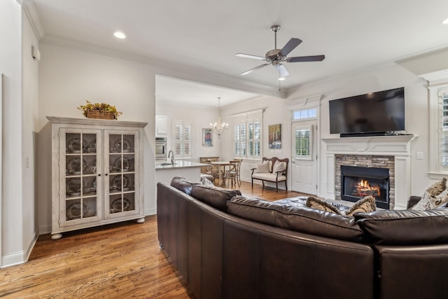 living room featuring ceiling fan with notable chandelier, sink, light wood-type flooring, a fireplace, and ornamental molding