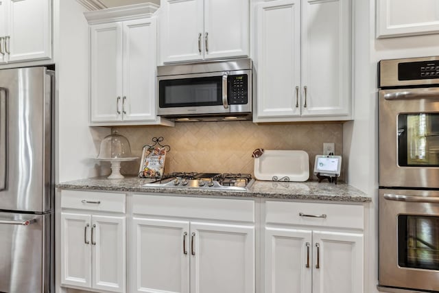 kitchen featuring light stone countertops, appliances with stainless steel finishes, decorative backsplash, and white cabinetry