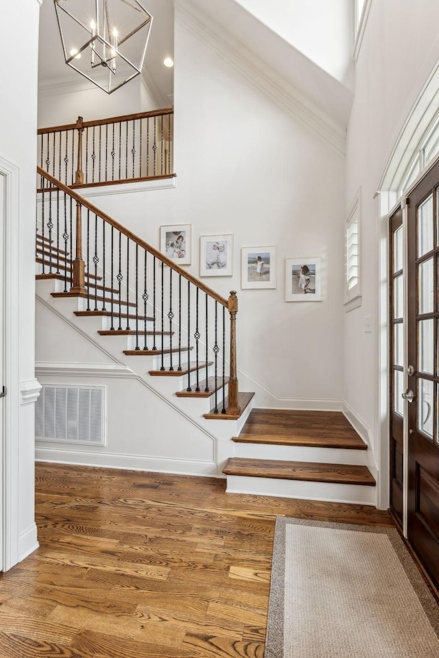 foyer featuring a notable chandelier, wood-type flooring, crown molding, and a towering ceiling