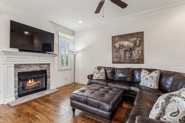 living room with a stone fireplace, ceiling fan, wood-type flooring, and ornamental molding