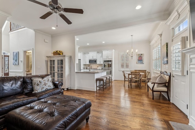 living room with ceiling fan with notable chandelier, ornamental molding, and dark wood-type flooring