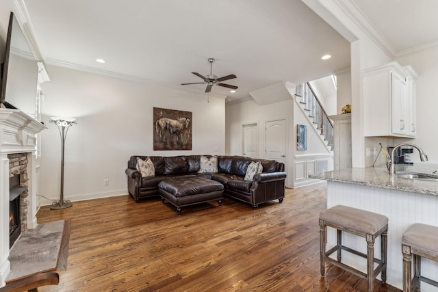 living room featuring crown molding, sink, ceiling fan, a fireplace, and dark hardwood / wood-style flooring