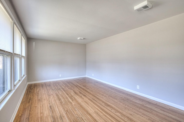 empty room with visible vents, light wood finished floors, and baseboards