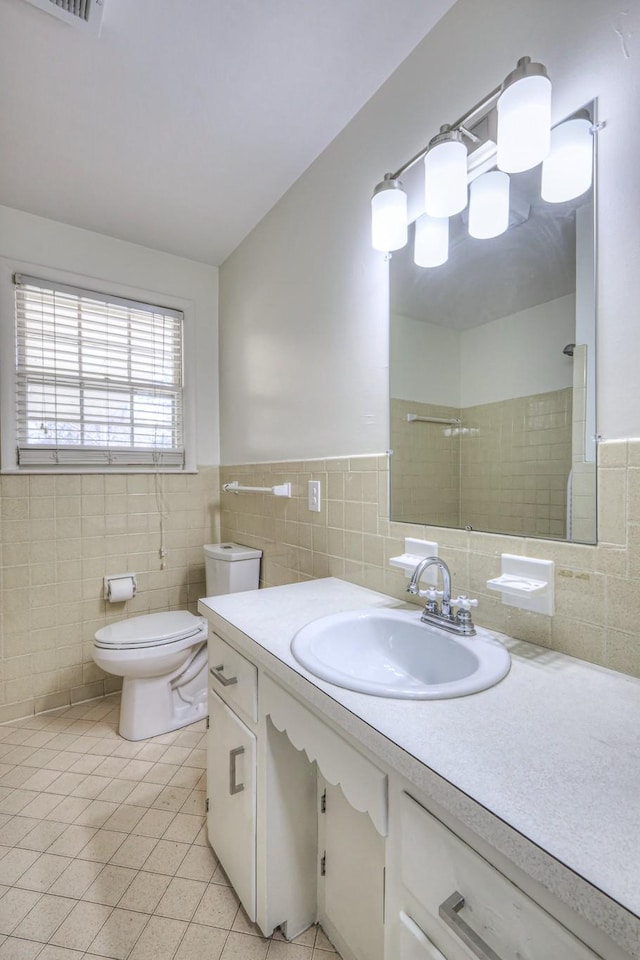 bathroom with tiled shower, toilet, tile patterned flooring, vanity, and tile walls