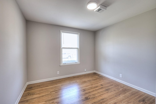 empty room with baseboards, visible vents, and wood finished floors