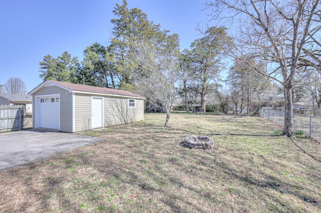 view of yard with aphalt driveway, an outbuilding, fence, a garage, and a fire pit